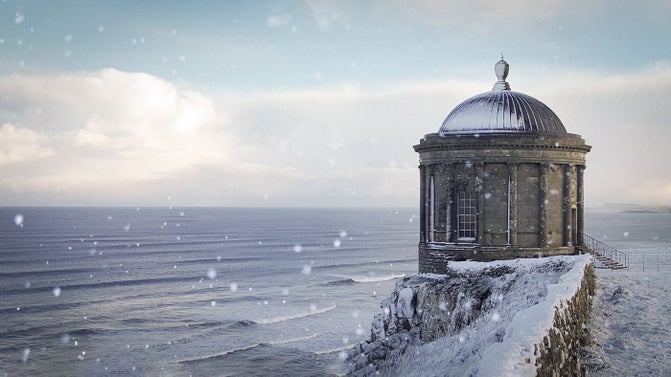 High above the crashing Atlantic waves, the iconic Mussenden Temple stands on the edge of the snow-covered cliffs of Downhill Demesne.